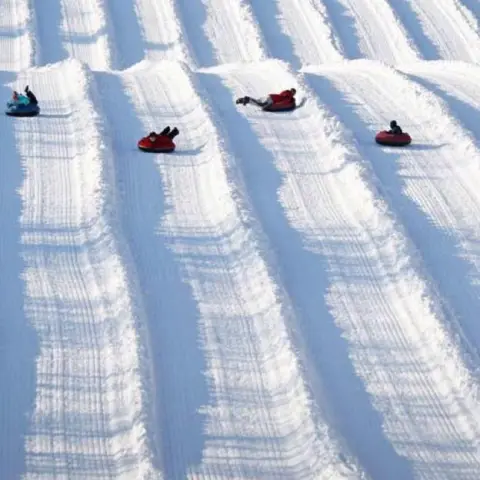 People snow tubing down parallel snowy lanes on a hill.