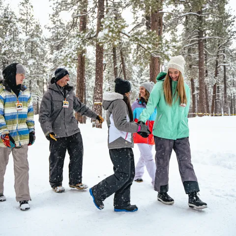 Group of people in winter clothes walking and laughing in a snowy forest.