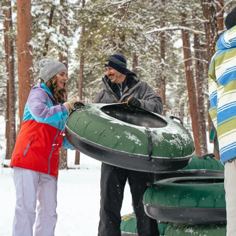 People in winter clothing holding inflatable snow tubes in a snowy forest.